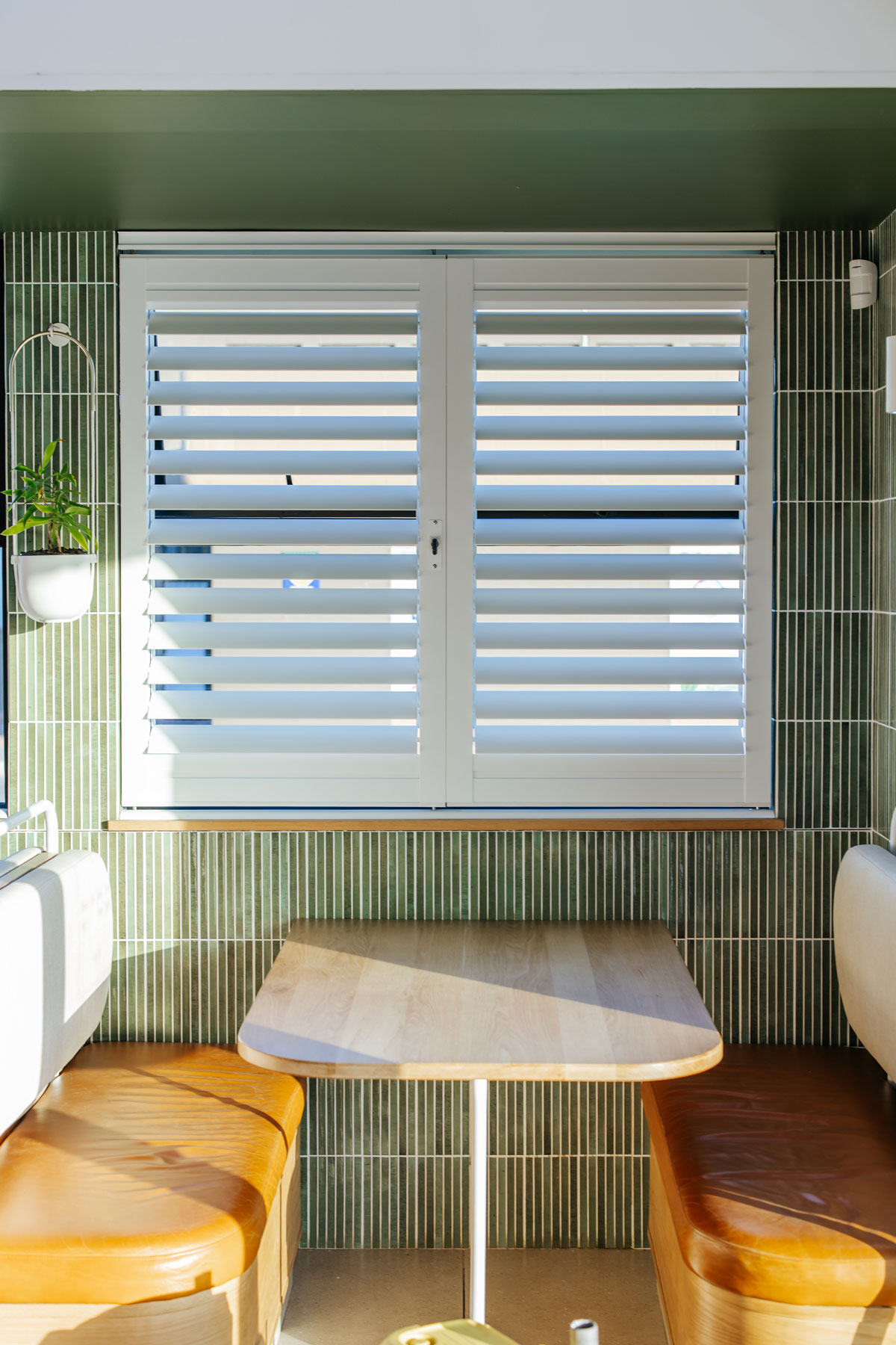 White shutters in a green-tiled booth at Plato Coffee